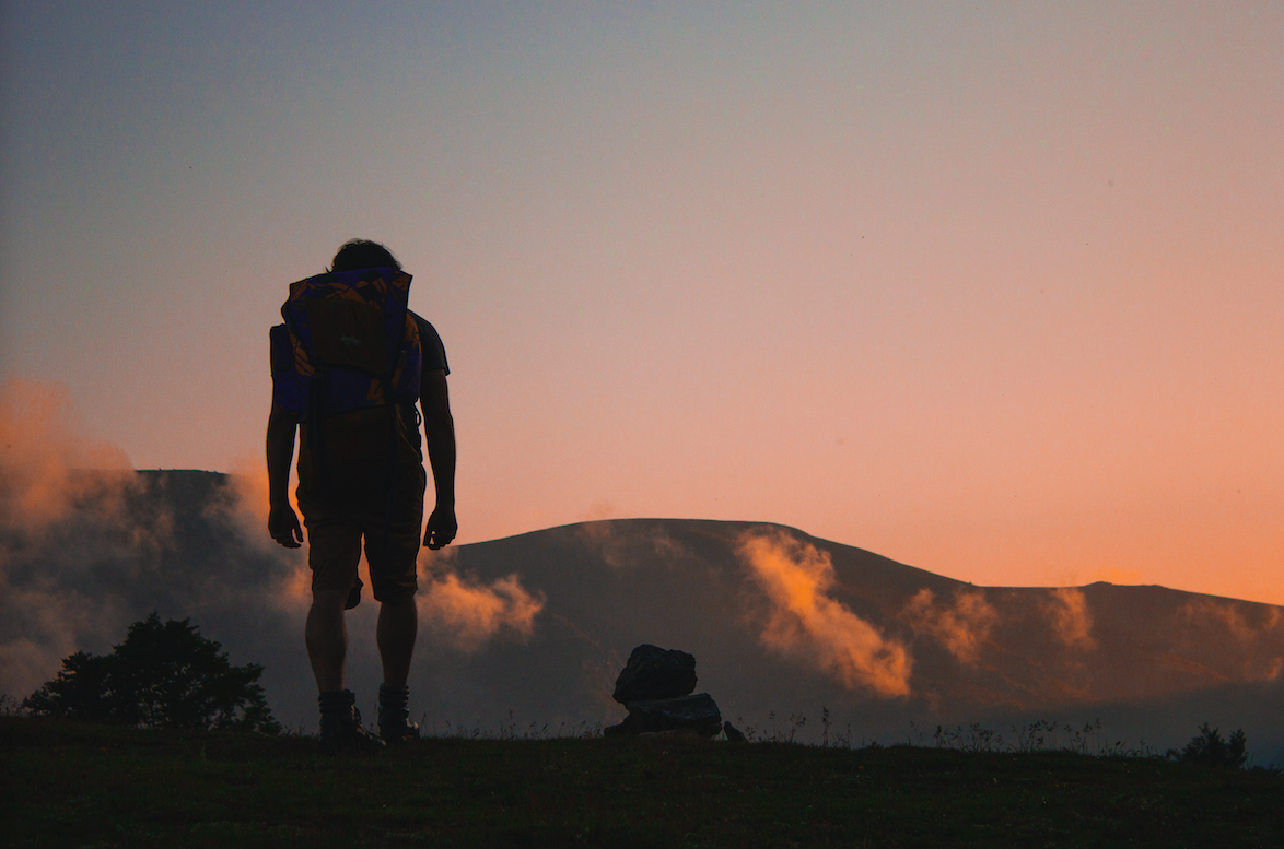 silhouette of a person wearing a hiking backpack hiking in the mountains at sunrise