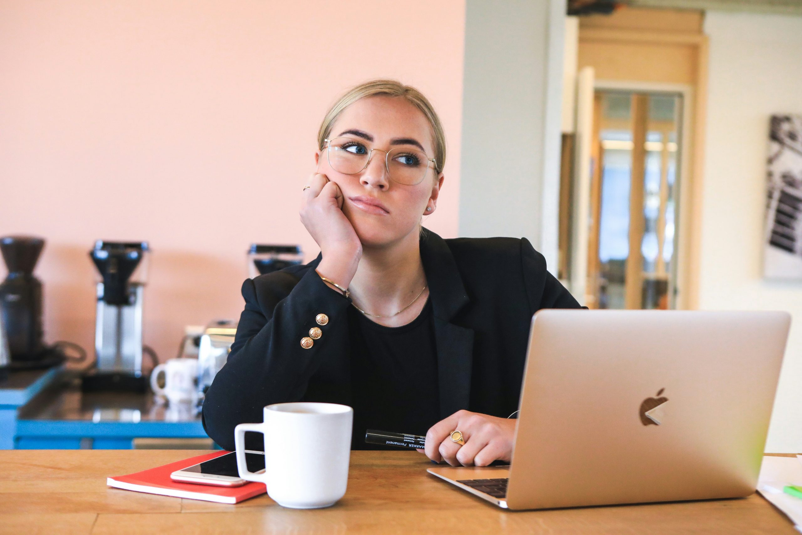 bored looking blonde woman wearing glasses sitting in front of a computer